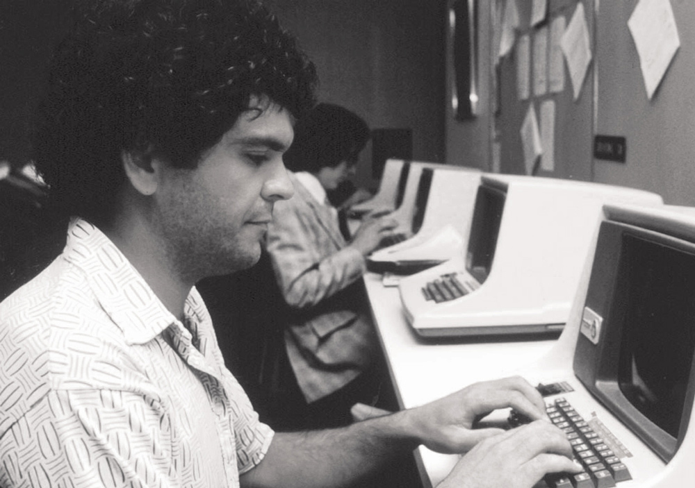 black and white image of a man sitting a computer in a computer lab