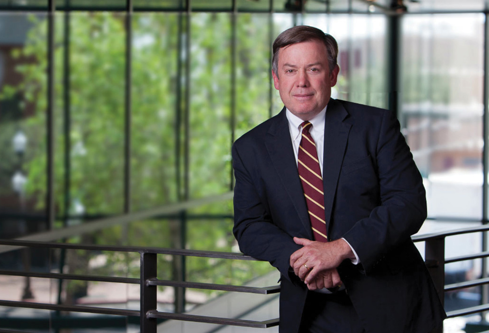 Michael Crow is a black suit and a striped tie