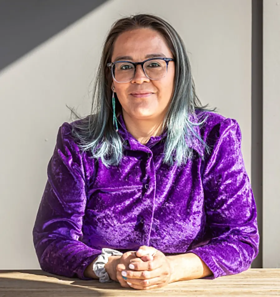 Portrait photograph of ASU alum Jessica Stago (BS Economics ’01) grinning in a dark purple velvet blouse with her hands closed crossed over each other; Jessica is the co-founder of Change Labs; Photo by Charlie Leight/ASU News