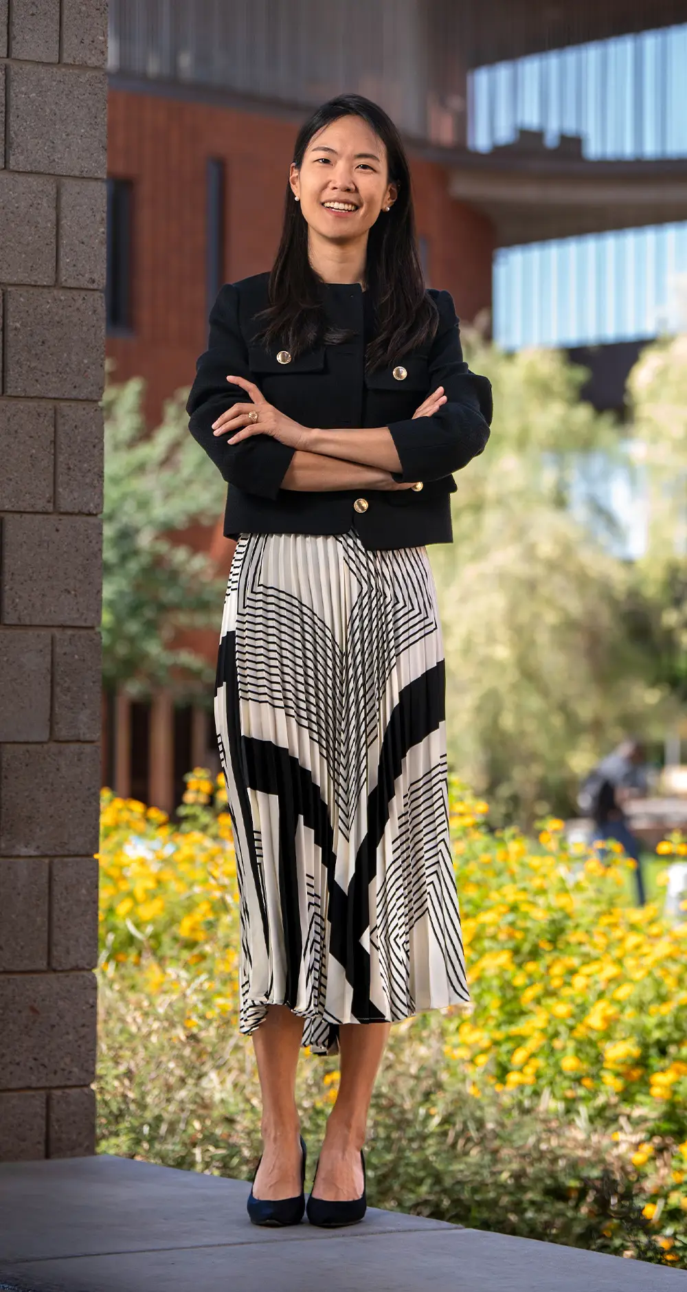 Seoin Yoon wearing a black suit jacket and black and white midi skirt crossing her arms and smiling while standing outdoors