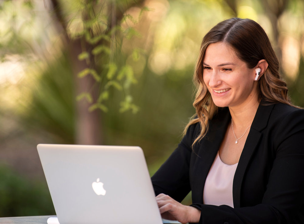 woman smiling while wearing earbuds and typing on a laptop