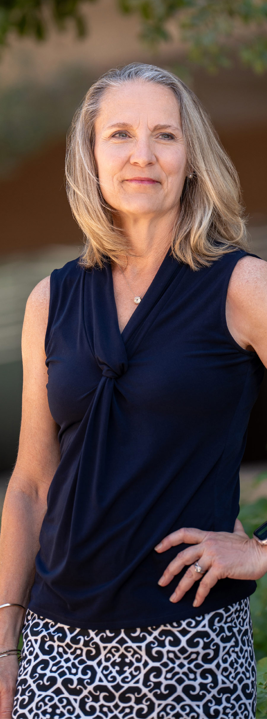 Pam Brooks standing with hand on hip smiling while wearing navy tank top with a front twist and black and white skirt on underneath