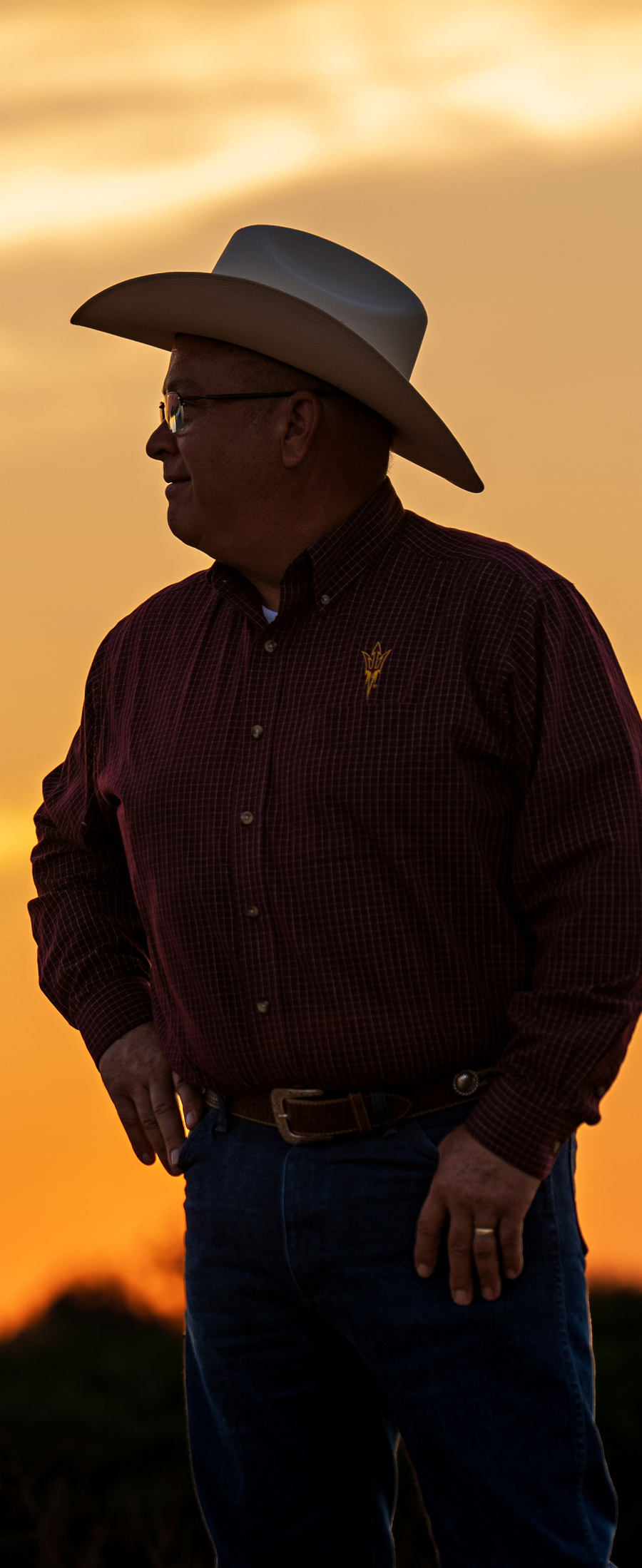 man wearing cowboy hat, long sleeve button up, and belt on denim jeans during sunset