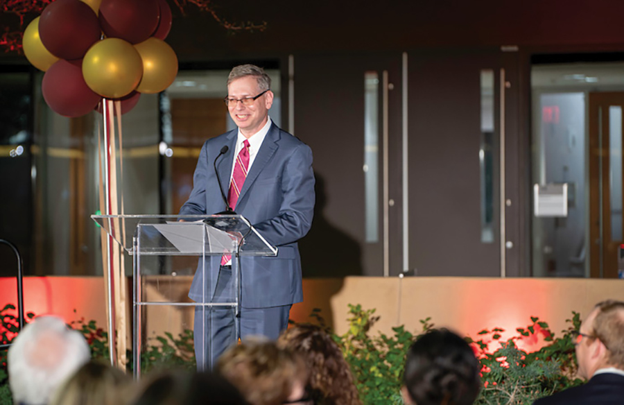 A man wearing glasses and a suit speaking at a podium during an event.