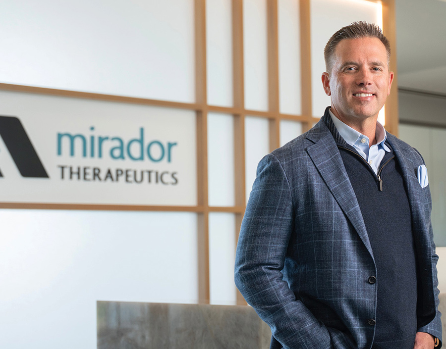 Man in a blue plaid jacket smiling in front of a Mirador Therapeutics sign.