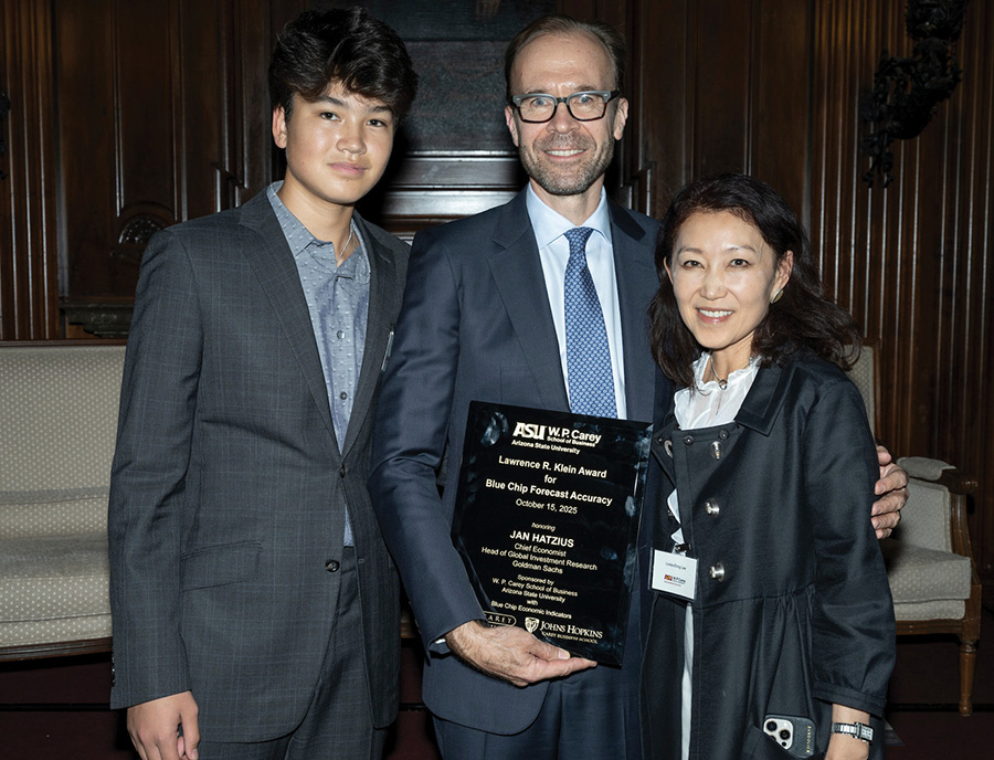 Man holding a Lawrence R. Klein award plaque posing alongside two family members.